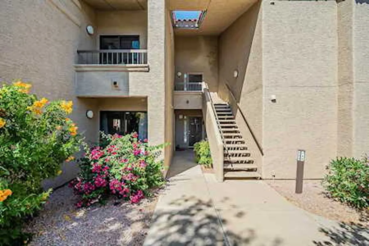 A view of balconies framed by vibrant flowers and a staircase, with a lush garden foreground. The scene hints at the inviting experience of enjoying morning coffee on the balcony or an evening stroll surrounded by greenery, capturing the seamless blend of indoor-outdoor living.