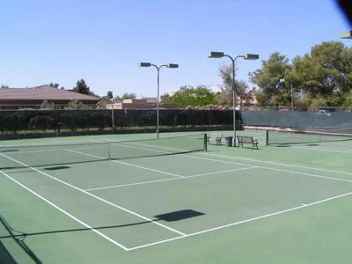 A well-maintained tennis court with benches and floodlights, set against an open sky. The space is designed for both active play and casual spectating, capturing the spirit of friendly competition and athleticism.