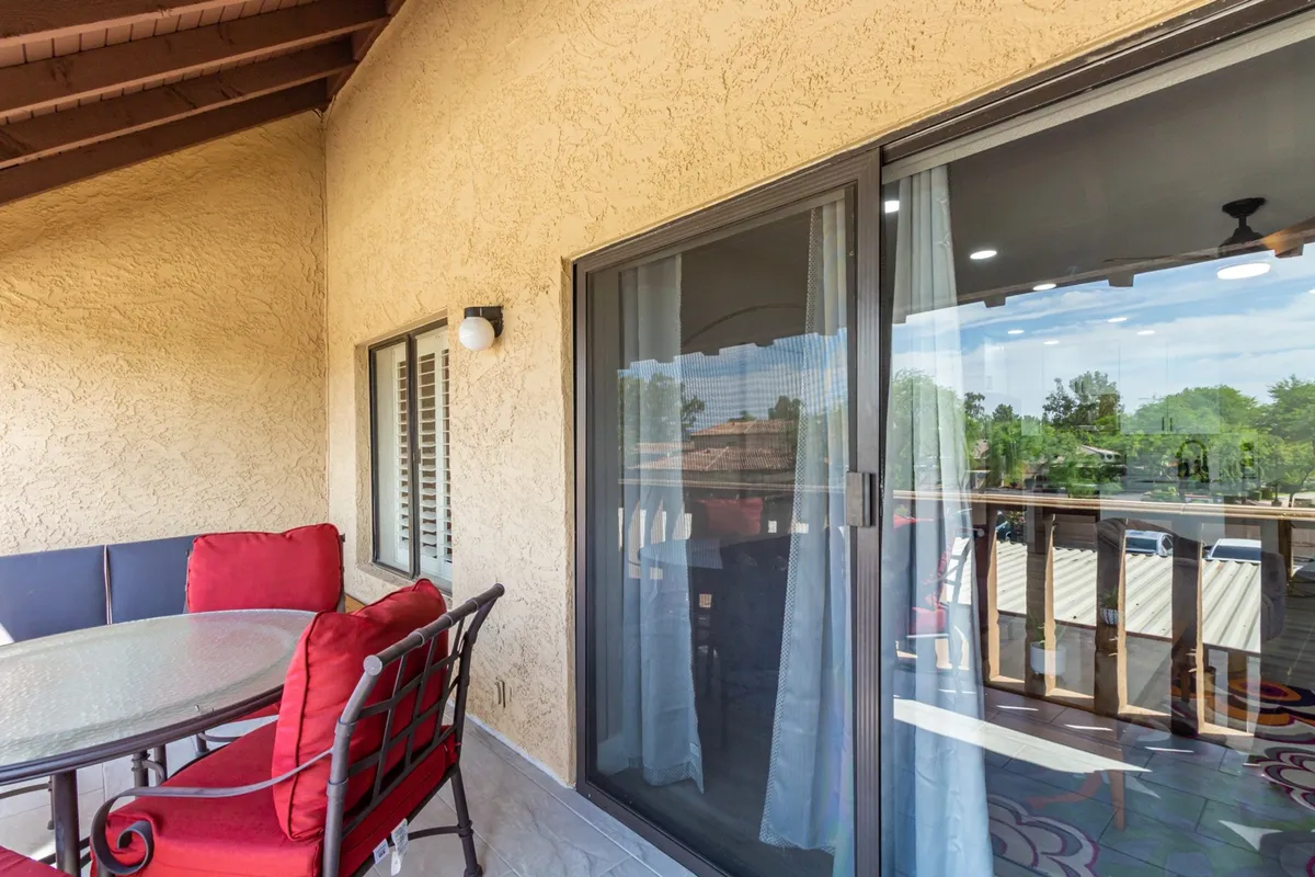 A cozy exterior seating area on a balcony or patio, featuring a glass sliding door, decorative floor tiles, and ample seating for friends or family. The atmosphere is comfortable and social, with the space set up for both casual lounging and enjoying meals or drinks while taking in the fresh air.