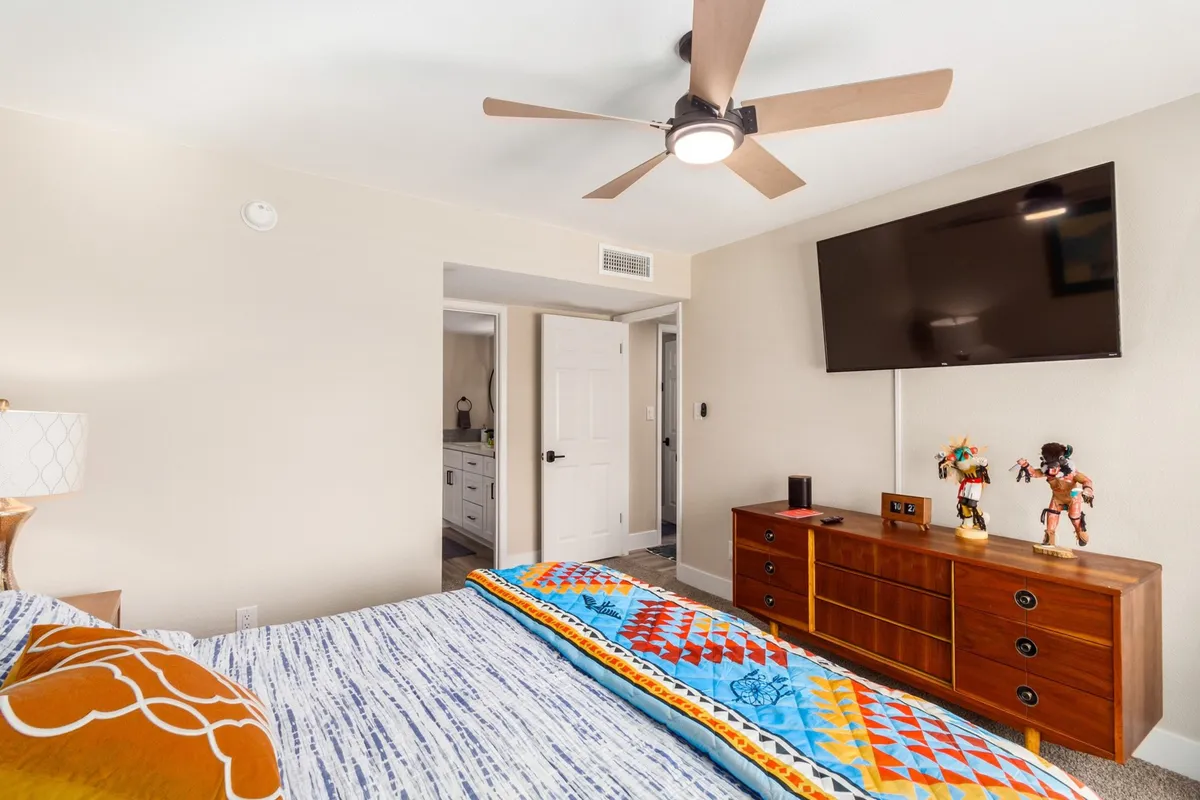 A tranquil king bedroom featuring a plush bed adorned with a colorful blanket, a wall-mounted smart TV, and a wooden dresser with decorative accents. The atmosphere is calm and restful, perfect for unwinding at the end of the day.