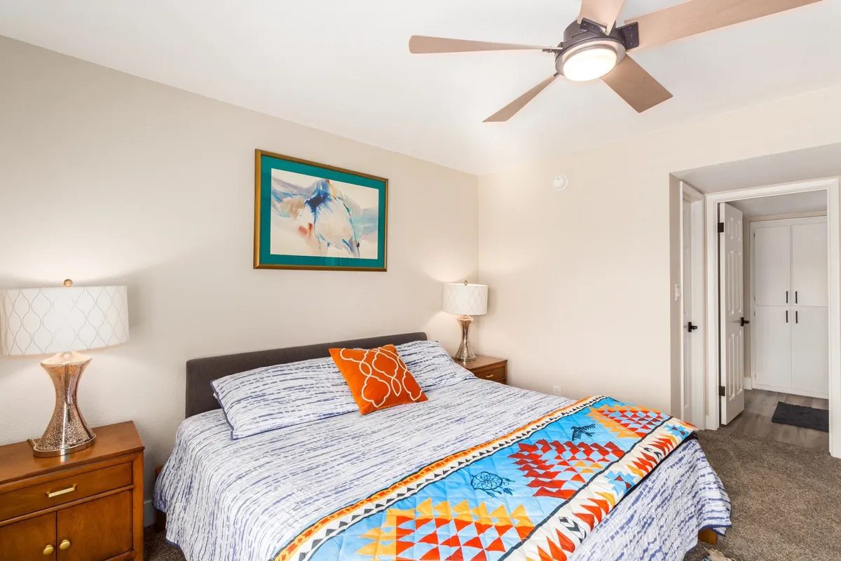A serene bedroom featuring a bed with colorful bedding, tasteful artwork, and soft lighting from bedside lamps. The peaceful setting offers a comfortable retreat, perfect for recharging after a demanding day.