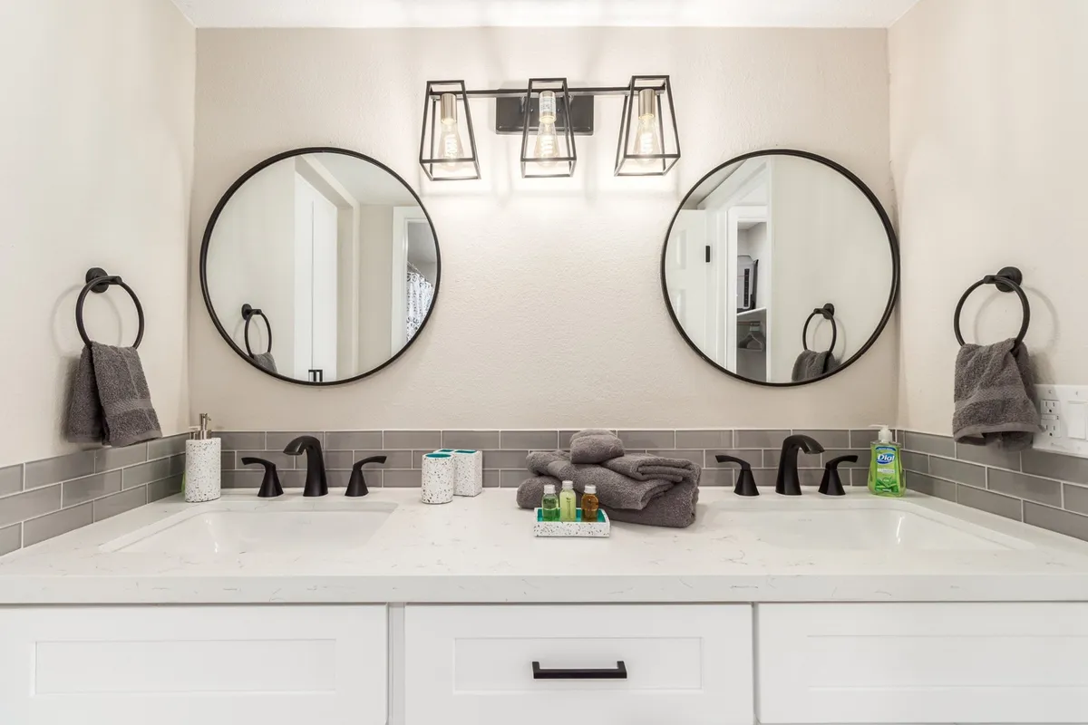 A bright and inviting bathroom featuring double sinks, round mirrors, and stylish lighting. The design is fresh, modern, and spacious, evoking the feel of a spa-inspired ensuite.
