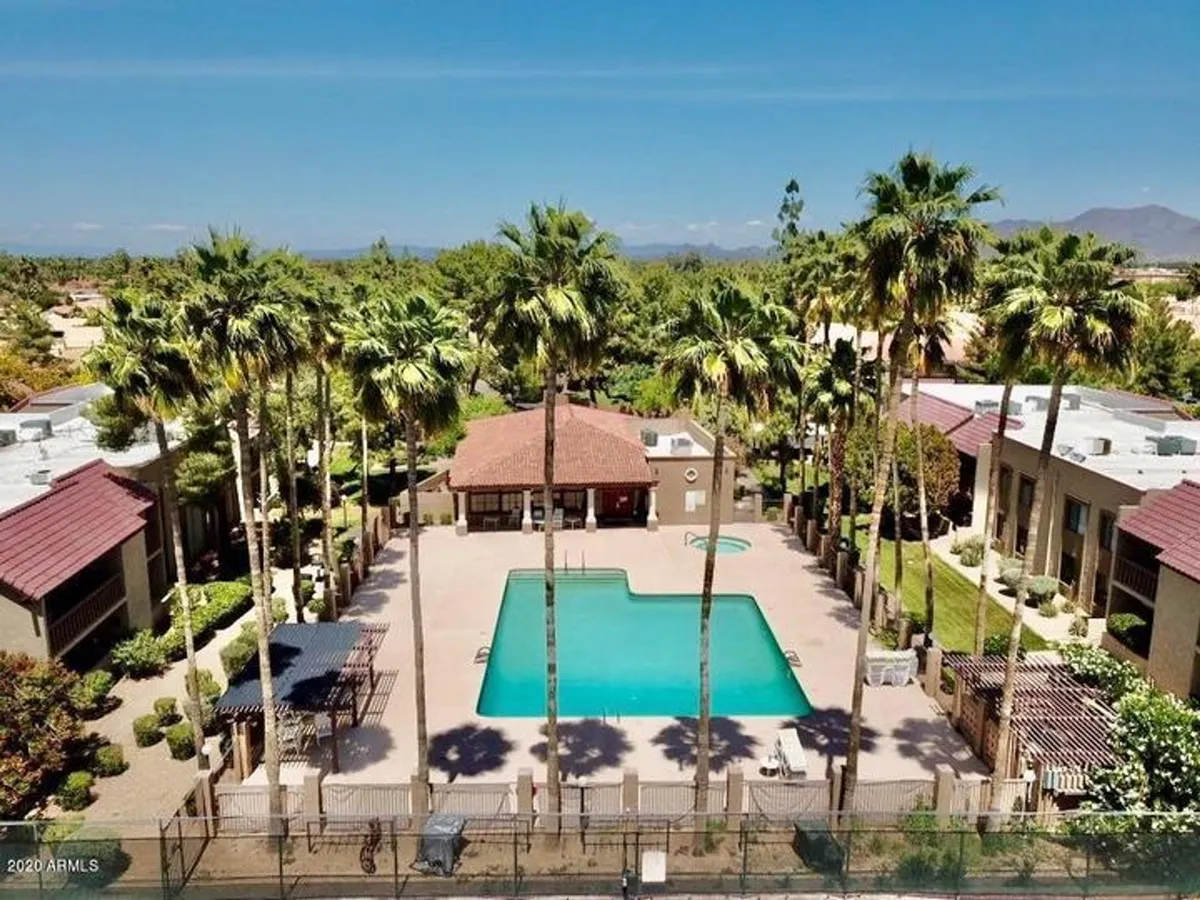 A sparkling swimming pool surrounded by palm trees and a community center, set amidst landscaped gardens. The area invites residents to socialize, sunbathe, swim, or gather for community events.